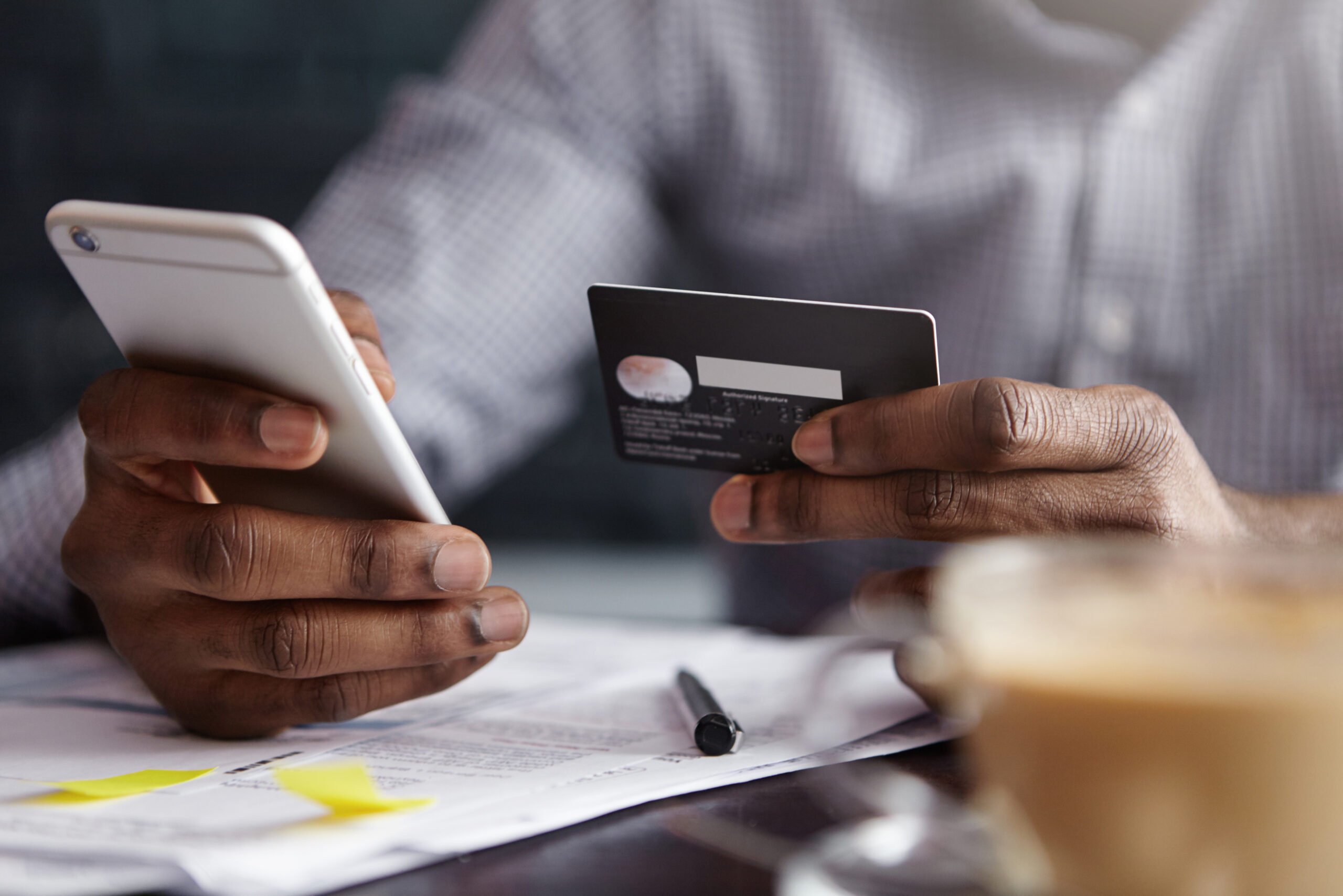 Cropped shot of African-American businessman paying with credit card online making orders via Internet. Successful black male holding plastic card making transaction using mobile banking application Cropped shot of African-American businessman paying with credit card online making orders via Internet. Successful black male holding plastic card making transaction using mobile banking application